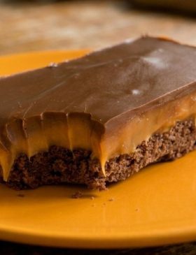 Quadrados da torta de manteiga escocesa do Pica-Pau, mostrando a base de chocolate, o recheio de caramelo espesso e o topo de chocolate ao leite brilhante.